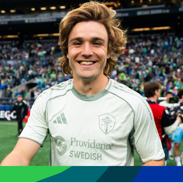 Pedro de la Vega, a smiling, blond young man in a Sounders uniform with stadium crowd in the background