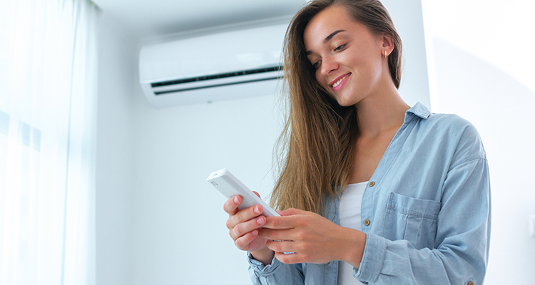 A smiling woman holding a remote control standing in front of a home heating wall unit