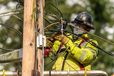 Line engineer wearing helmet, gloves and safety goggles, repairing a power line at the top of a pole